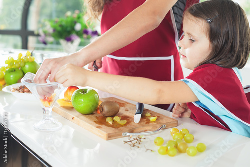 Cute little girl cooking with her mother. Healthy food, fruits