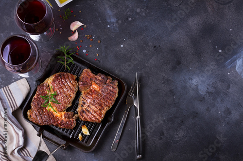 Obraz na płótnie Hot Grilled beef steak on dark background with two glasses of red wine