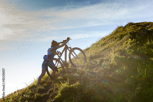 Obraz na płótnie Biker pushes bicycle up in the mountains