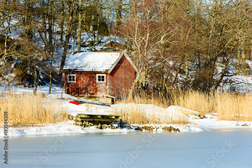 Red Wooden Boatshed In Winter Landscape Pier And Reed At Shoreline Woodland