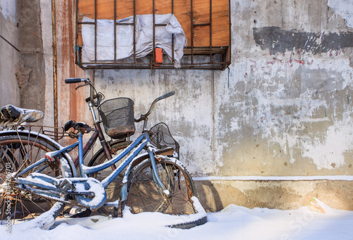 Plakat foto Snow covered old bicycles against a textured wall, Changchun, China