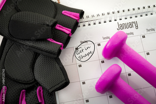New year resolution and the desire to get in shape concept with a calendar with january first circled, gym equipment like purple dumbbells and pink and black workout gloves