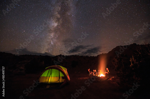 Family of four sitting around a campfire under stars and the milky way.