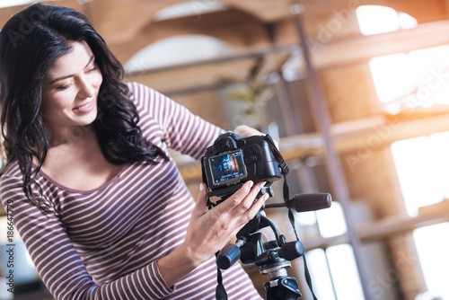 Preparation for video shooting. Cheerful nice young woman looking at the camera screen and smiling while preparing to shoot a video