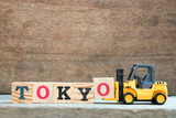 Yellow toy forklift hold letter block O to complete word Tokyo on wood background