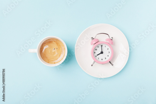 Morning cup of coffee and alarm clock on blue working desk top view. Breakfast time concept. Flat lay style.