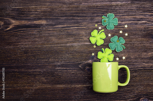Green mug with four-leaf clover on wooden background. Copy space.