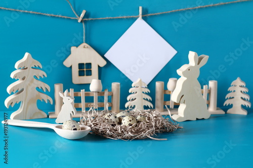 composicion-de-pascua-con-huevos-de-codorniz-tarjeta-blanca-y-figuras-de-madera-sobre-un-fondo-azul