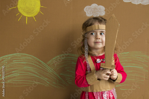 Portrait of a playful baby with a cardboard sword and a suit. handmade. background of painted sun and white clouds