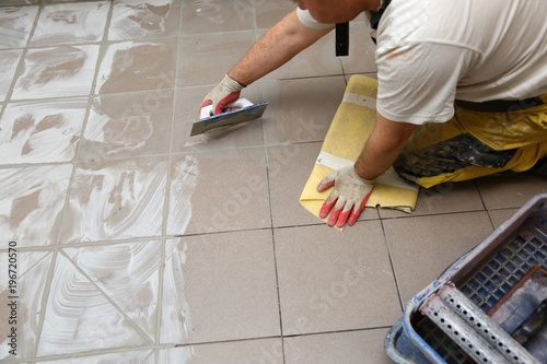 Grouting ceramic tiles on the floor by a man. © fotodrobik