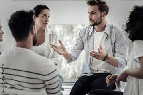 Group therapist. Nice pleasant young man looking at the group members and speaking to them while telling his story