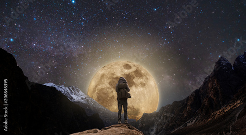 a man standing on mountain peak at night, and full moon on night sky full of stars