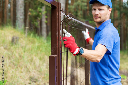 worker installing welded metal mesh fence © ronstik