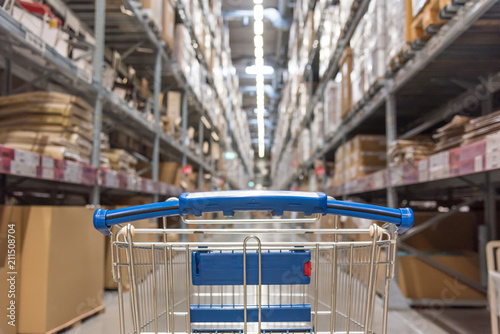 Warehouse storage of retail merchandise shop. Trolley Shopping Cart Between Dry Grocery Shelf Section in Supermarket Warehouse Retail Outlet as Shopping Concept.