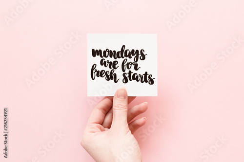 Minimal composition on a pink pastel background with girl's hand holding card with quote - Mondays are for fresh starts
