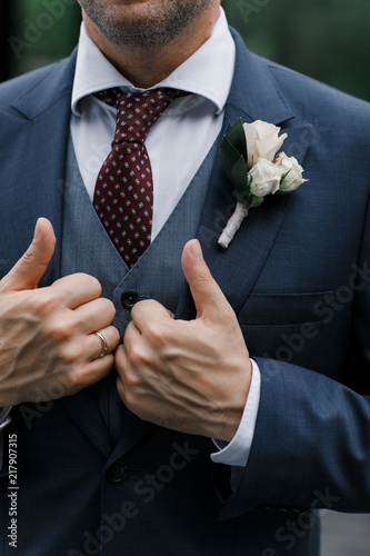 Groom in blue tuxedo and bowtie hold his hands on jacket. Wedding. Details © shumovdenis