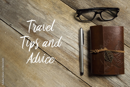 Top view of eyeglasses,pen and notebook on wooden background written with TRAVEL TIPS AND ADVICE.
