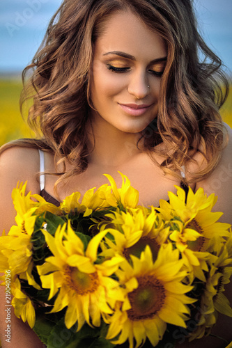 Young beautiful woman wearing a hat in a field of sunflowers © Natali