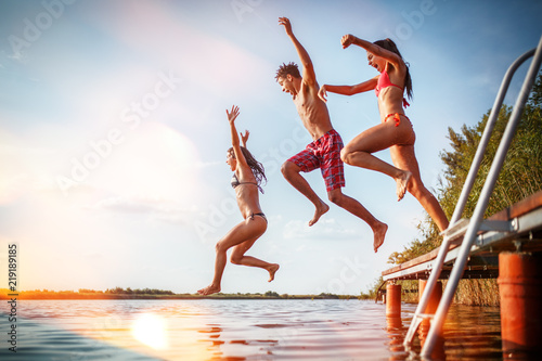 Group of friends jumping into the lake from wooden pier.Having fun on summer day. © SolisImages