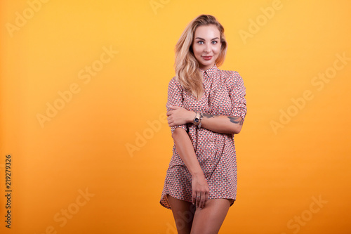 Attractive young blonde woman in short dress in studio over yellow background © DC Studio