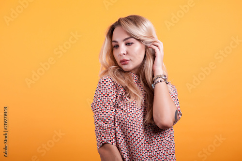 Beautiful young woman in short dress playing with her hair in studio over yellow background © DC Studio