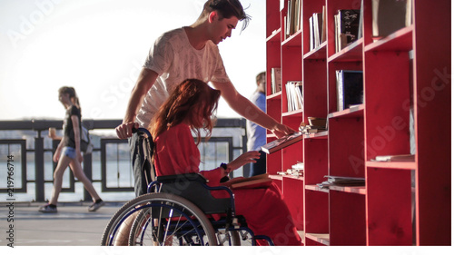 A young man shows books to his girlfriend with red hair, who is sitting in a wheelchair © Barselona Dreams