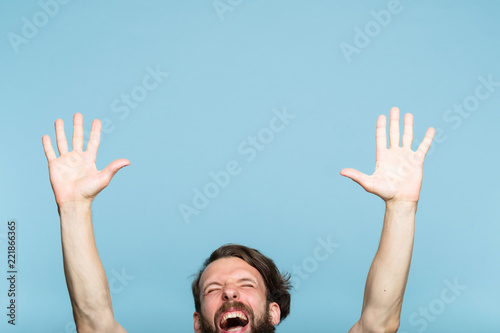 happiness enjoyment and laugh. excited man with hands in the air. portrait of a young bearded guy on blue background. emotion facial expression. feelings and people reaction. © golubovy
