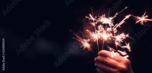 Hand holding burning Sparkler blast on a black bokeh background at night,holiday celebration event party,dark vintage tone