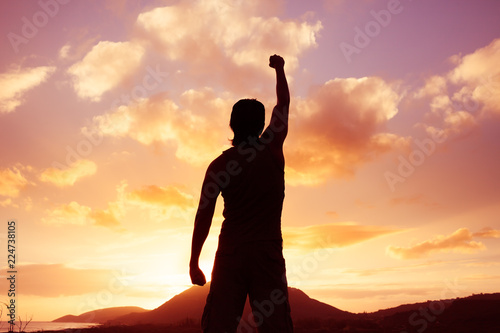 Young motivated man standing on mountain with fist in the air.