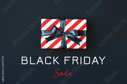 Gift box wrapped in red striped paper and tied with black bow on black background. Black friday concept, top view.