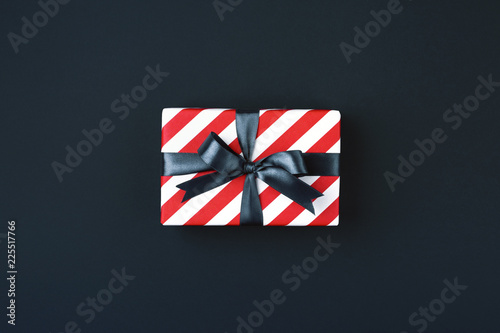 Gift box wrapped in red striped paper and tied with black bow on black background. Black friday and cyber monday concept, top view.
