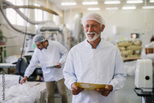 Father and son checking products in their food factory. Mature man in sterile clothes standing in front of the camera with smile on his face.Successful business concept.