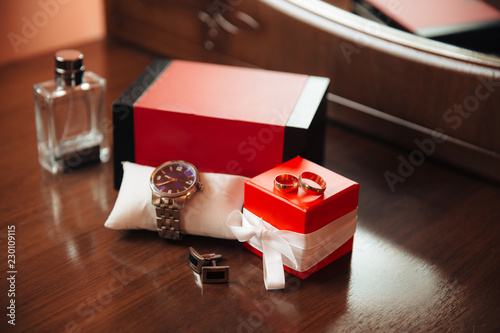 Men's watches, perfume, wristwatches, golden rings and cufflinks on the background of a brown table. Clothing accessories businessman. Concept of grooms accessories at wedding day. © romannoru