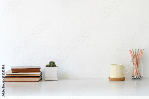 Workspace coffee mug, books, pencil and cactus on white desk.