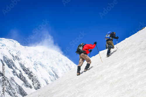 Two mountain trekkers on steep snowed hill with peaks background © Martin M303