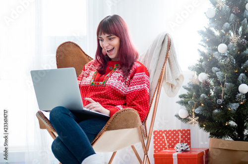 Young woman using laptop next to xmas tree, Christmas shopping online © leszekglasner