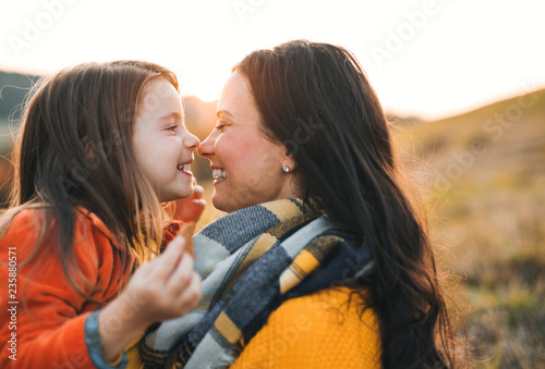 A portrait of young mother with a small daughter in autumn nature at sunset.