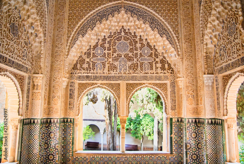 Moorish architecture in one room of the Nasrid Palaces of the Alhambra of Granada in Spain, with beautiful intricate carvings and windows overlooking a garden. © Brigida Soriano