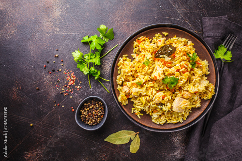 Rice with chicken in a black plate on a dark background, top view.