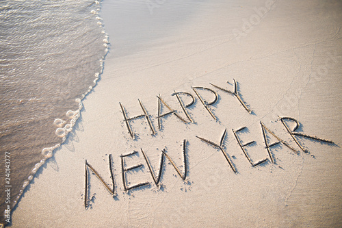 Happy New Year message handwritten in smooth, clean sand with a fresh wave coming up the beach © lazyllama