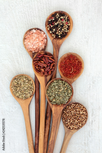 Herb and spice food seasoning in olive wood spoons with fennel, himalayan salt, chili peppers, peppercorns, herbs de provence, saffron, and mustard seed. Left to right on rustic wood. Top view. © marilyn barbone