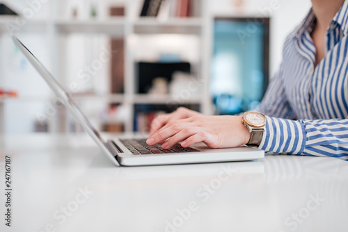 Woman sitting at desk and working at laptop computer, close-up, copy space. © bnenin