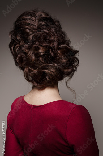 Back view of unrecognizable female turned back at camera. Woman in red dress after beauty salon with stylish haircut. Dark gray studio background. © Вячеслав Косько