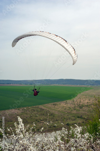 Paraglider flies over the fields and the blooming mountainside in the spring season. Paragliding over the spring fields and meadows near the Dniester River in Ukraine. © Viktoria