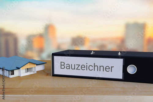 Haus-Planung. Akten-Ordner beschriftet mit dem Wort Bauzeichner liegt neben einem Haus-Modell auf einem Schreibtisch. Skyline einer Stadt im Hintergrund. © sharpi1980