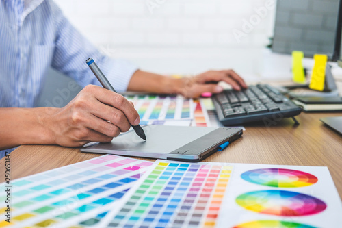 Image of male creative graphic designer working on color selection and drawing on graphics tablet at workplace with work tools and accessories in workspace © Freedomz