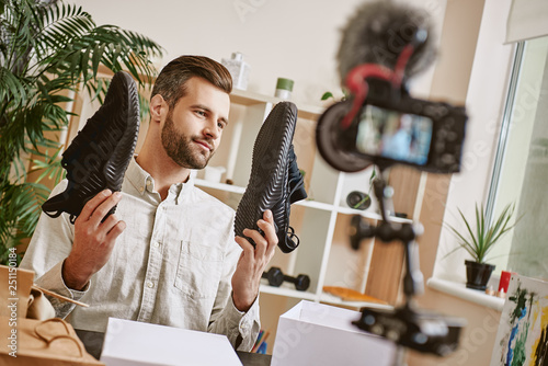 Popular fashion blogger. Young male fashion blogger holding stylish sneakers while making new content for his fashion blog.