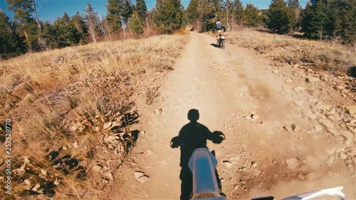 Motorcycle rider follows brother down golden dirt trail in green California forest pov extreme action lifestyle © skichef