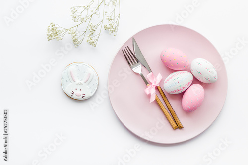 Easter dining table in pastel colors. Plate, cutlery, painted eggs, gingerbread and dry flower branch on white background top view space for text © 9dreamstudio