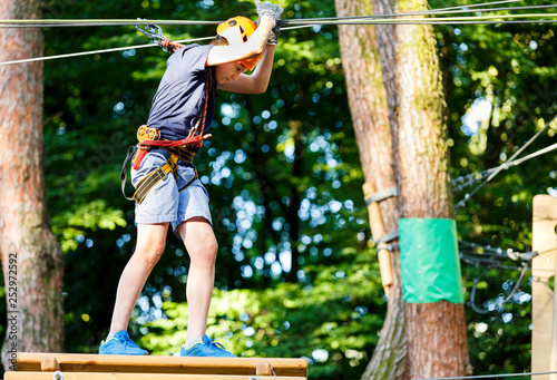 Cute young boy in helmet with climbing equipment in the rope amusement park. Summer camp, holidays concept